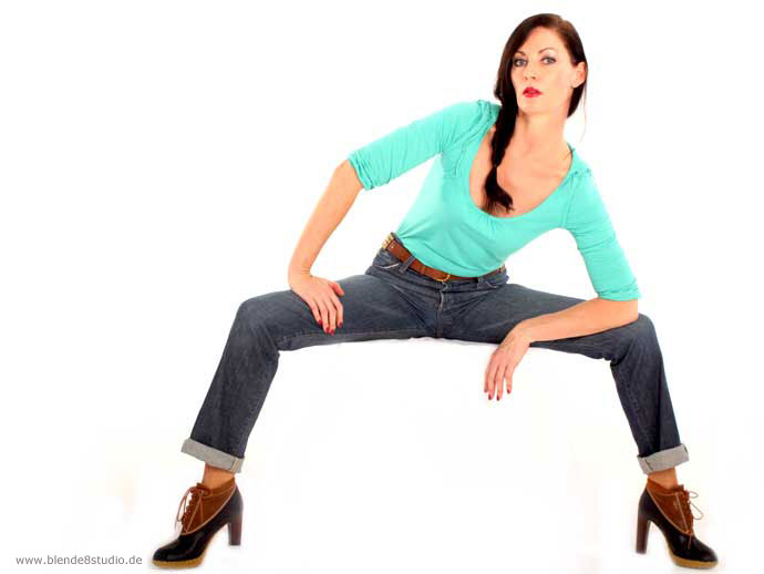 Model in t&uuml;rkisfarbenem Oberteil und Jeans in einer dynamischen Ganzk&ouml;rperpose